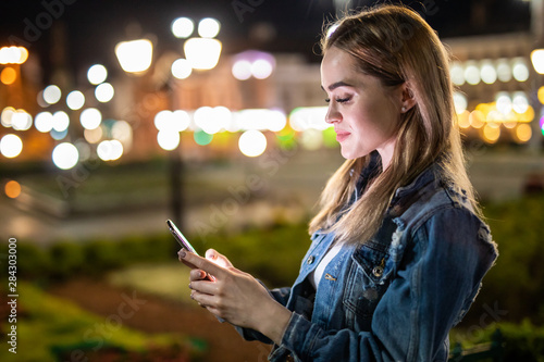Outdoor portrait of beautiful young woman using her mobile phone at night.