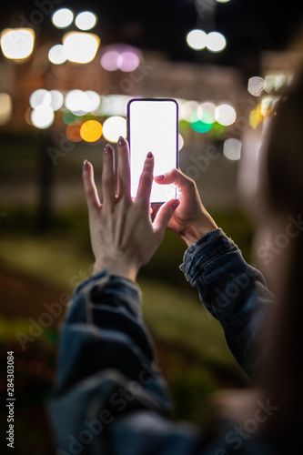 Woman pointing finger on blank screen smartphone on background bokeh light in night atmospheric city