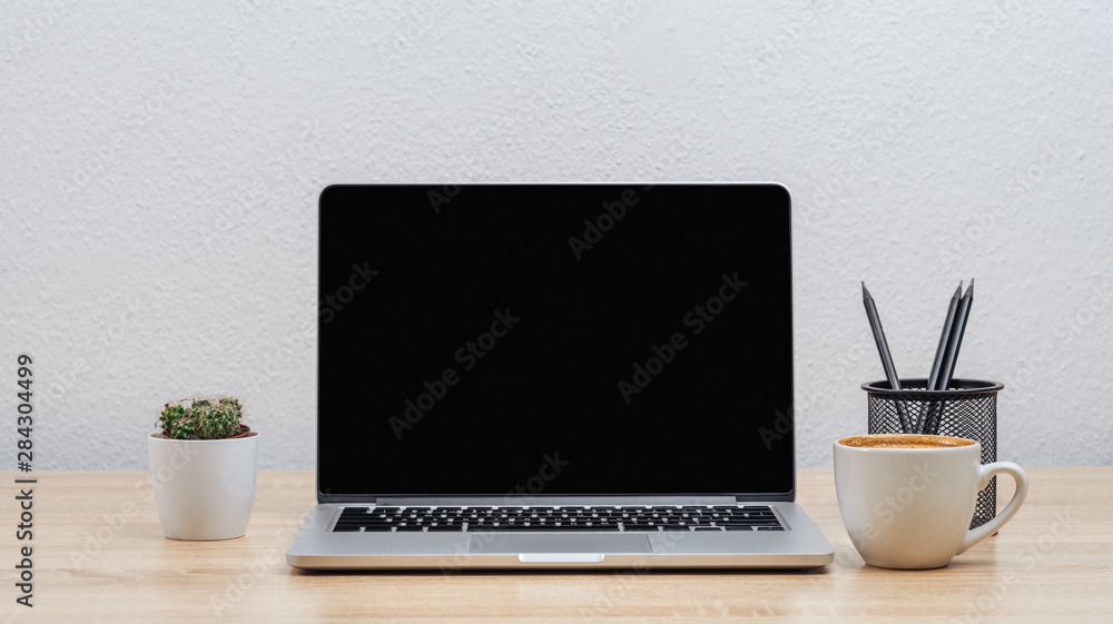 Dark laptop screen on an office desk with various items, on a white wall background.Mockup. Dark laptop screen on an office desk with various items, on a white wall background.Mockup.
