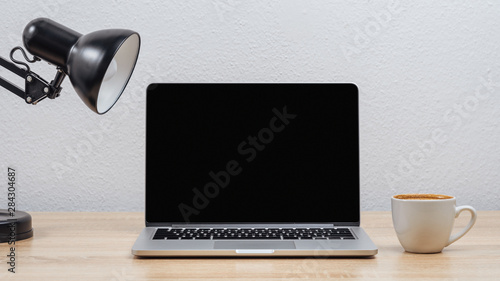 Open laptop screen on a desktop with a cup of coffee on a white wall background.Mockup.