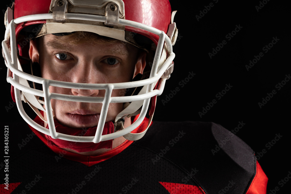 American football player in helmet standing against black background