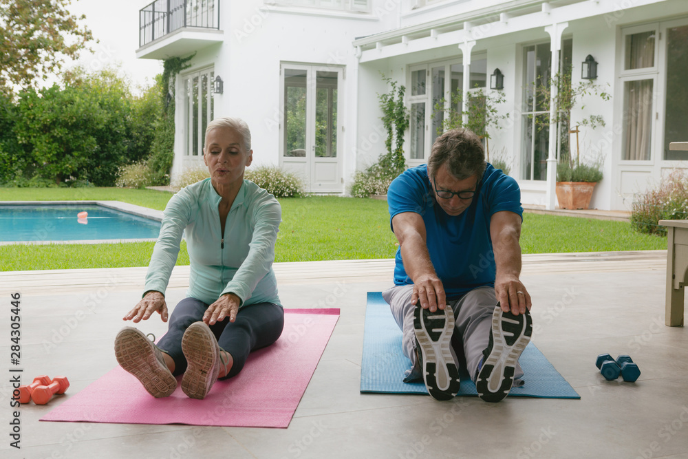 Active senior couple doing stretching exercise in the porch at home