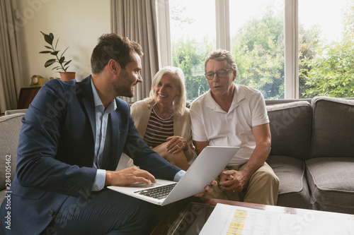 Active senior couple discussing with real estate agent over laptop in living room photo