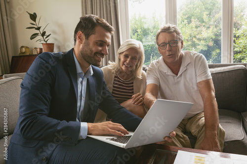 Active senior couple discussing with real estate agent over laptop in living room photo