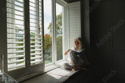 Active senior woman looking through window at home