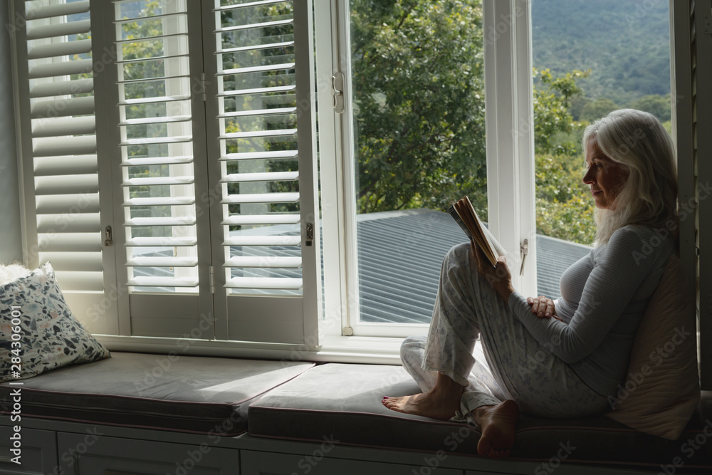 Active senior woman reading a book on window seat Active senior woman reading a book on window seat