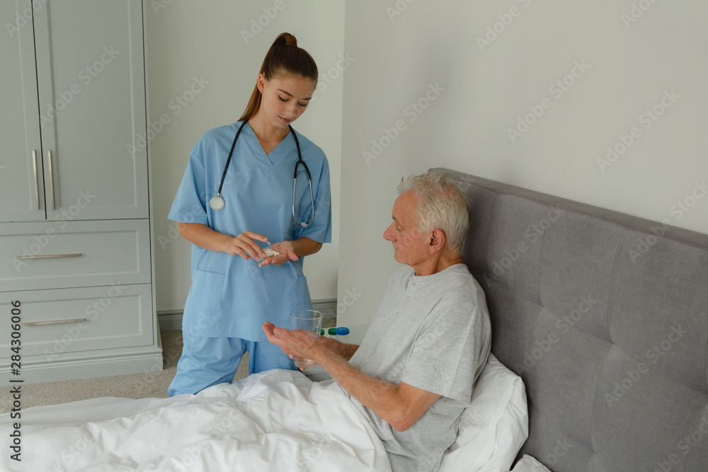 Fototapeta premium Female doctor giving medicine to active senior patient in bedroom