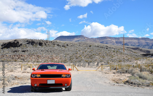Fast red orange sport muscle car with burning lights in cloudy weather near mountains © Lunatishe
