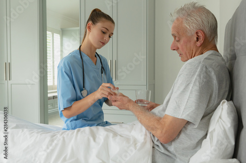 Schilderij op canvas Female doctor giving medicine to active senior patient in bedroom