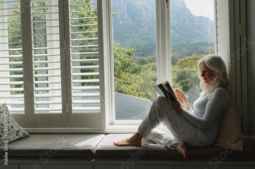 Active senior woman reading a book on window seat Free Download Active senior woman reading a book on window seat - GFXLoad