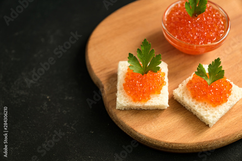 Delicious red caviar on wheat bread served with parseley on wooden desk. Copy space for your text