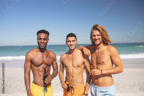 Male friends holding beer bottles and looking at camera on the beach