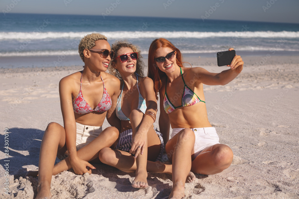 Female friends taking selfie with mobile phone on the beach