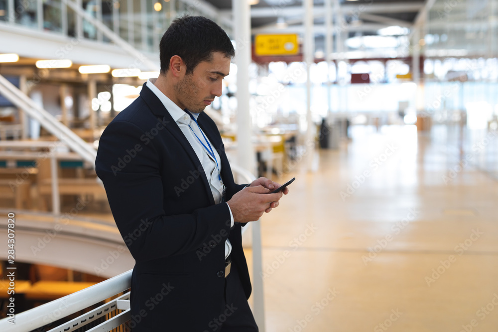 Businessman leaning on railing and using mobile phone in a modern office Businessman leaning on railing and using mobile phone in a modern office