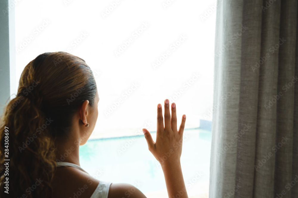 Thoughtful woman looking through window in living room at home Thoughtful woman looking through window in living room at home
