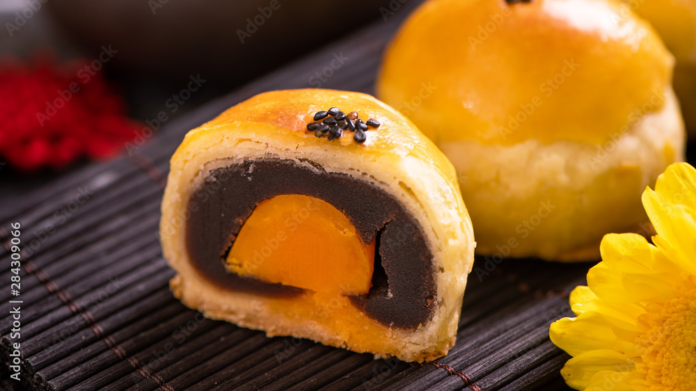 Tasty baked egg yolk pastry moon cake for Mid-Autumn Festival on black slate dark background. Chinese festive food concept, close up, copy space.