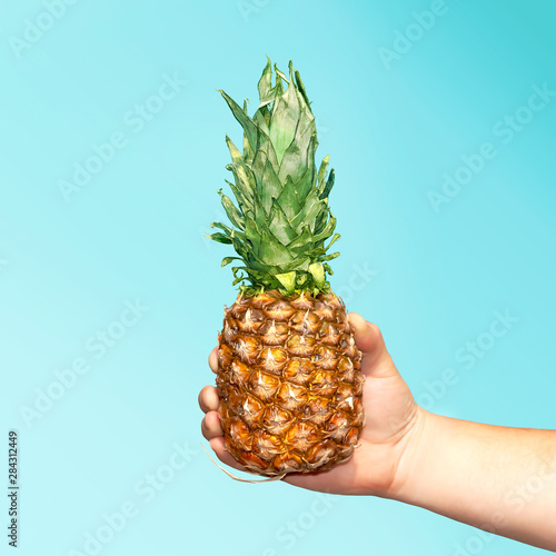 Hand holding a pineapple. Creative layout made of pineapple. Food concept. Shine color.