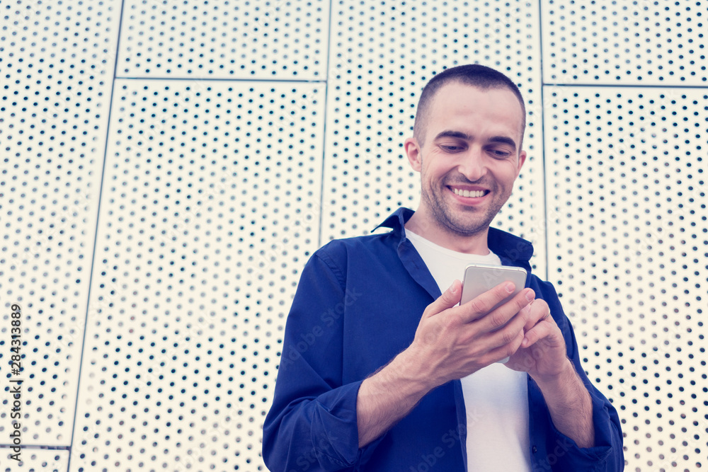 Happy attractive man with the smartphone in his hands, he's smiling and looking at his phone, front view Happy attractive man with the smartphone in his hands, he's smiling and looking at his phone, front view