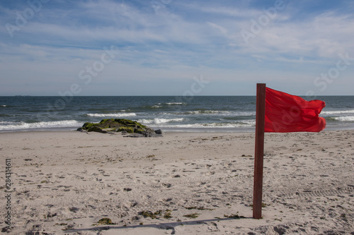 Warning sign of a red flag at a beautiful beach with a blue sky , Long Beach, New York, USA
