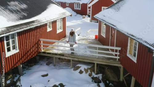 girl standing next to the traditional multicolored wooden fishing house rorbu on a sea shore at Lofoten archipelago, nothern Norway