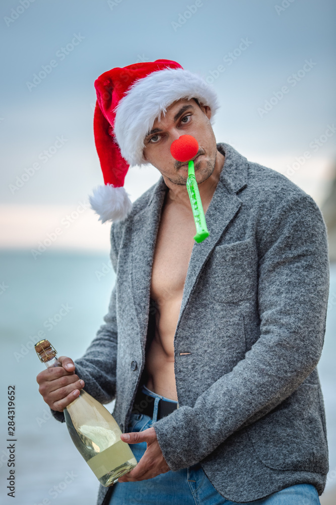 Obraz premium Man in Santa Claus red hat on the beach in morning hangover.