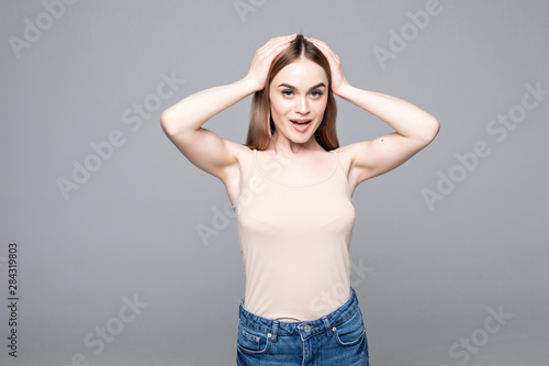 Just happy. Young smiling exited woman in casual wear holding hands on head and shouting while standing against gray studio background. Cheerful crazy girl with open mouth posing to camera © dianagrytsku