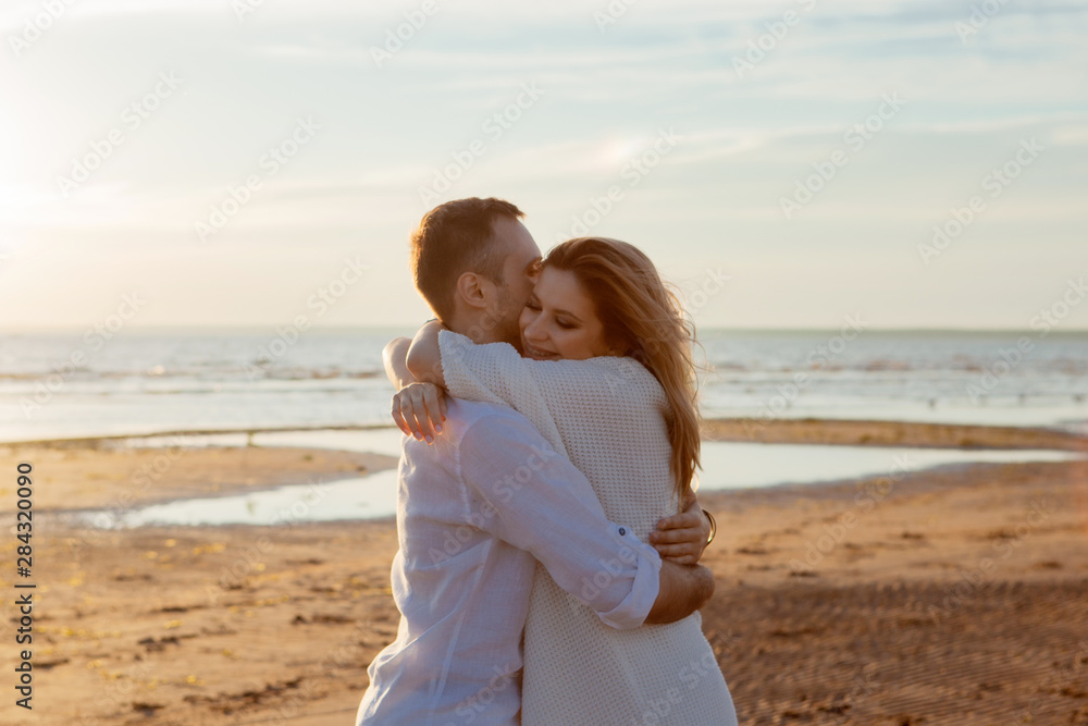 Love, sunset, romance. A young couple in long white soft clothes hugging against the backdrop of a calm sea, sunset. Love, sunset, romance. A young couple in long white soft clothes hugging against the backdrop of a calm sea, sunset.