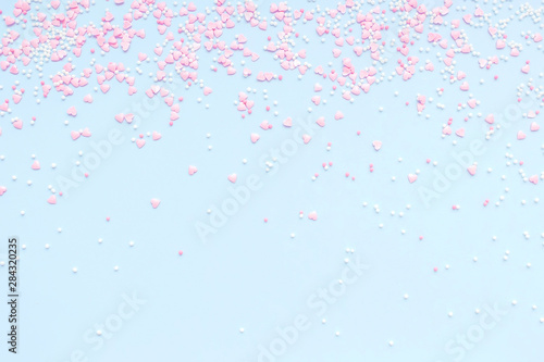 Festive romantic gentle abstract background for the design. Pink confetti in the shape of hearts on a blue background. Top view  flat lay composition. Copy space for text. 
