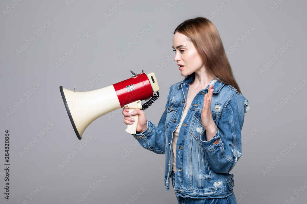 Young woman screaming in megaphone with arm isolated gray background Young woman screaming in megaphone with arm isolated gray background