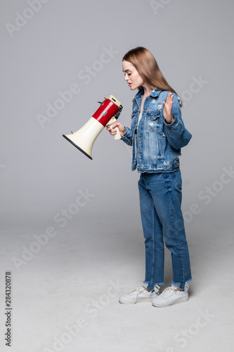 Young woman shouting through a megaphone to announce something isolated on gray background