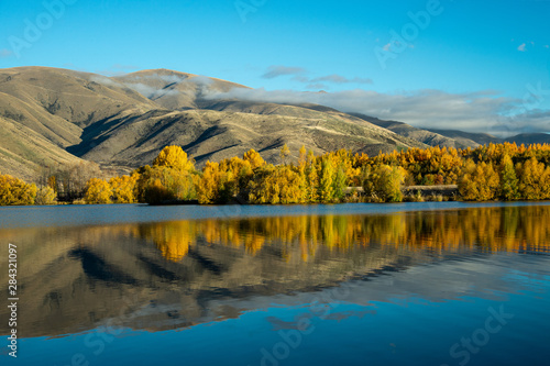 Marvelous scene of autumn season with yellow leaves trees, blue sky and dry mountain reflect in the turquoise - colored lake in Twizel, South Island New Zealand. © Jack Tamrong