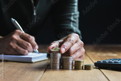 Men are Saint documents about save money and put coin in glass jar on desk on black background.