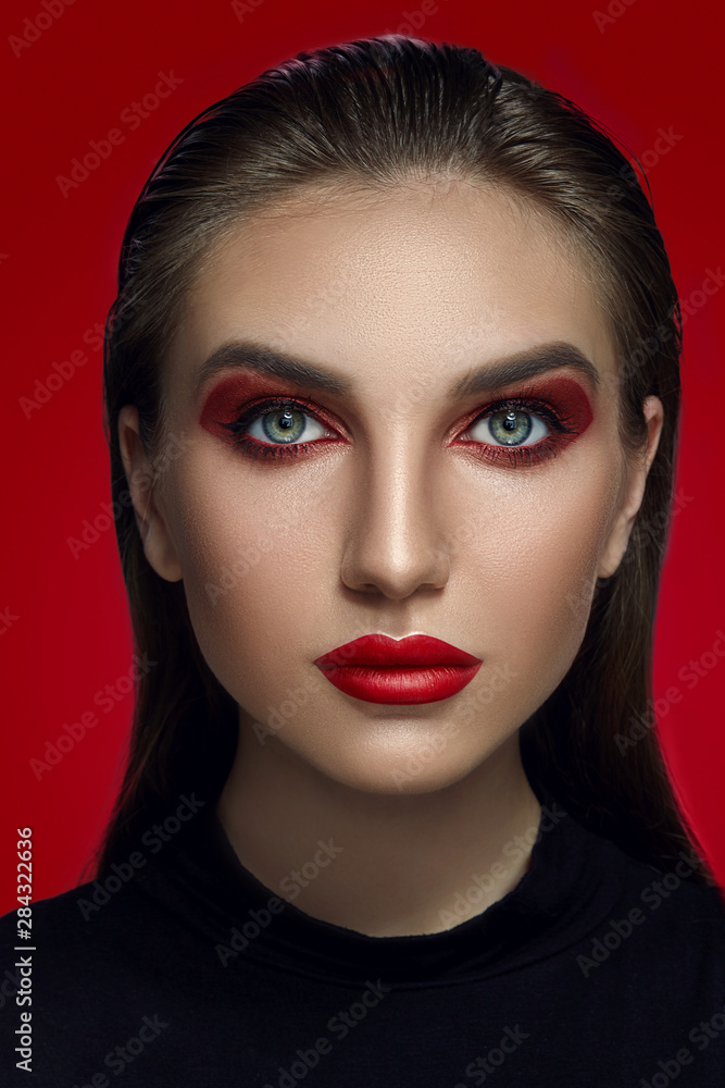 Close-up glamour portrait of a beautiful model with bright make-up posing over a red background.