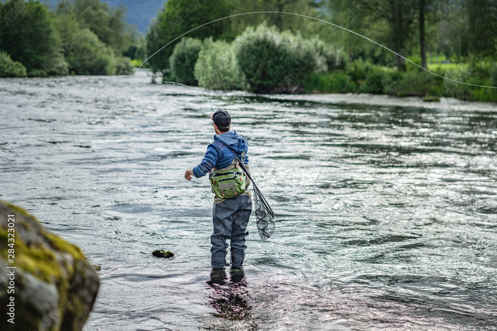 Angler mit Angel in Wathose im Wasser beim Fliegenfischen Angler mit Angel in Wathose im Wasser beim Fliegenfischen