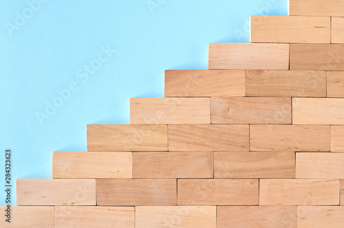 Brown wooden blocks stairs shape idea on blue background composition. © Sviatoslav Kovtun