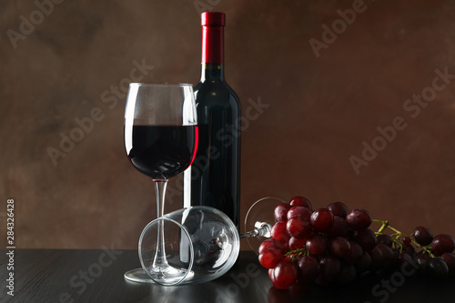 Grapes, bottle and glass with wine against brown background, copy space