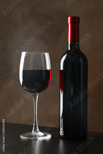 Bottle and glass with wine against brown background, copy space