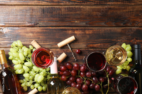 Flat lay. Grapes, corkscrew, bottles and glasses with wine on wooden table, copy space