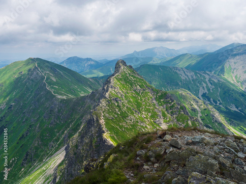 view from Ostry Rohac peak on Western Tatra mountains or Rohace panorama. Sharp green mountain peak placlive with hiking trail on ridge. Summer blue sky white clouds.