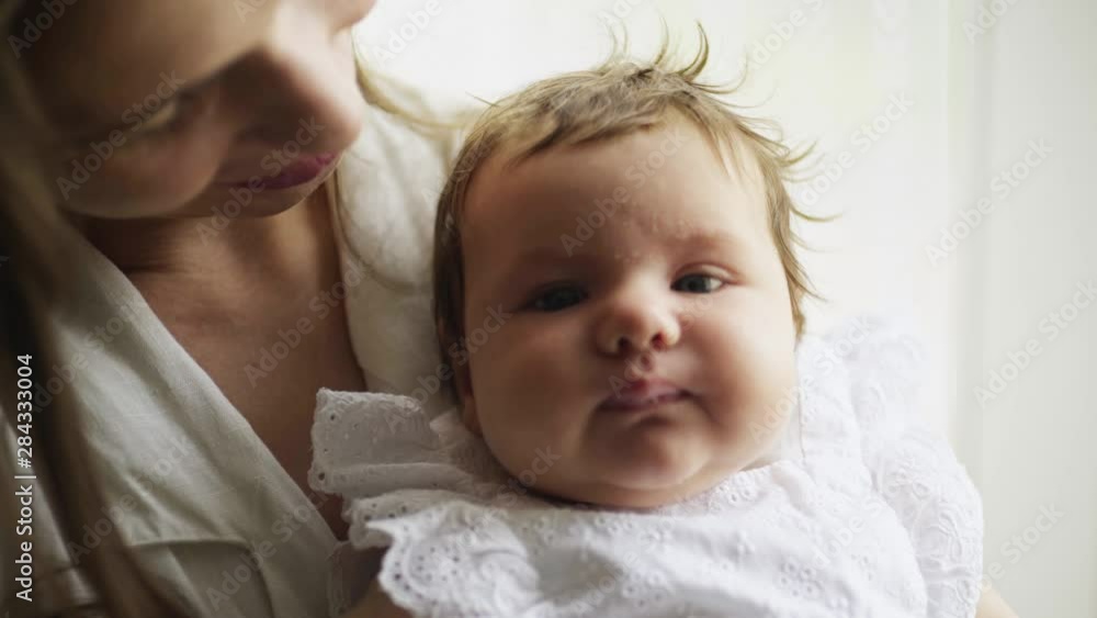 Young mother holding her newborn child near the window. Close-up portrait newborn baby nursing on hands. Woman and new born girl relax in a bedroom. Family at home Young mother holding her newborn child near the window. Close-up portrait newborn baby nursing on hands. Woman and new born girl relax in a bedroom. Family at home