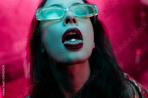 beautiful girl in sunglasses with lsd on tongue in nightclub