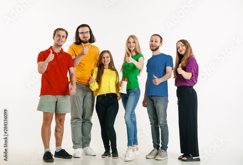 Young man and woman weared in LGBT flag colors on white background. Caucasian models in bright shirts. Look happy together, smiling and hugging. LGBT pride, human rights and choice concept.