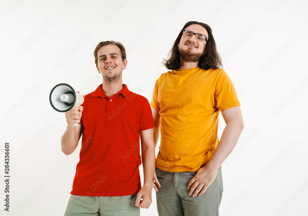 Young men weared in LGBT flag colors on white background. Caucasian male models in bright shirts. Look happy, smiling and hugging. LGBT pride, human rights and choice concept. Holding mouthpiece. Young men weared in LGBT flag colors on white background. Caucasian male models in bright shirts. Look happy, smiling and hugging. LGBT pride, human rights and choice concept. Holding mouthpiece.