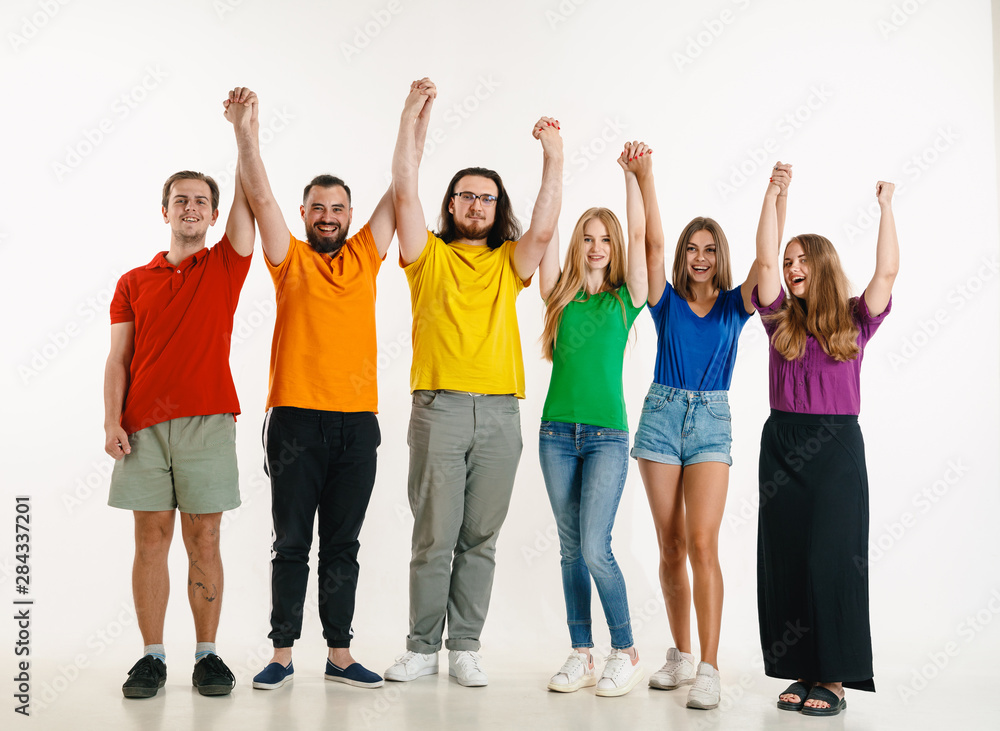 Young man and woman weared in LGBT flag colors on white background. Caucasian models in bright shirts. Look happy together, smiling, hugging. LGBT pride, human rights and choice concept. Celebrating.