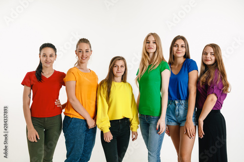Young man and woman weared in LGBT flag colors on white background. Caucasian models in bright shirts. Look happy together, smiling and hugging. LGBT pride, human rights and choice concept.