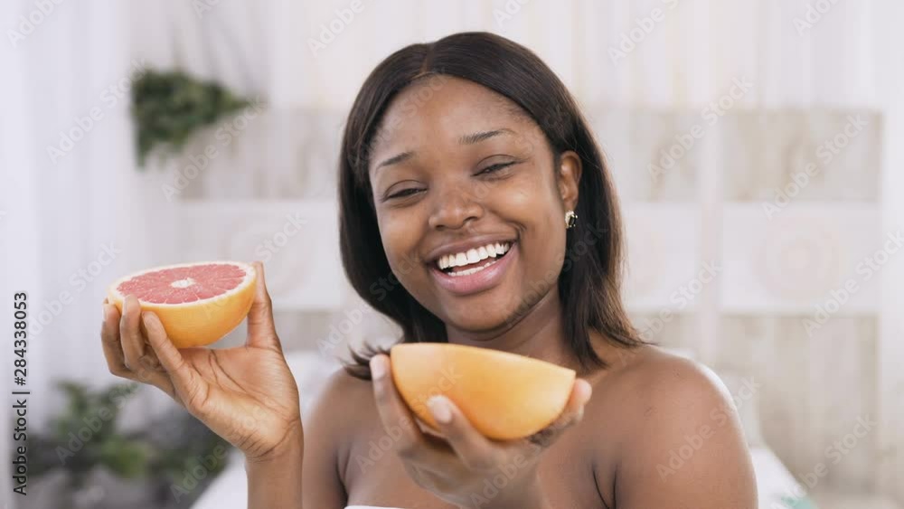 Portrait of happy african american woman holding pomelo halves smiling and enjoying natural skin care.Beautiful female with perfect complexion. Healthy skin care face concept Portrait of happy african american woman holding pomelo halves smiling and enjoying natural skin care.Beautiful female with perfect complexion. Healthy skin care face concept