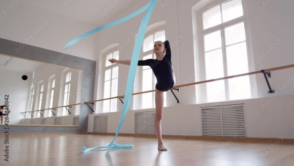 Wide shot of Caucasian female dancer wearing black leotard exercising with blue ribbon in studio Wide shot of Caucasian female dancer wearing black leotard exercising with blue ribbon in studio