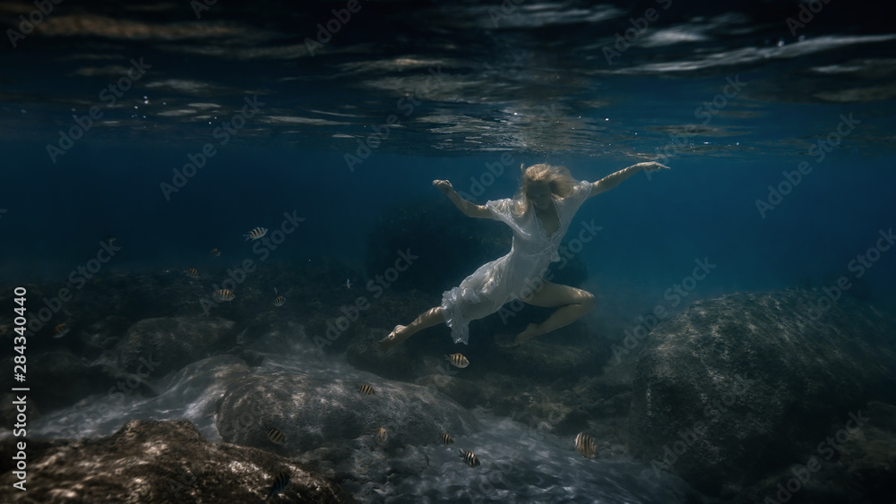 Obraz premium Woman in white swims underwater in the sea