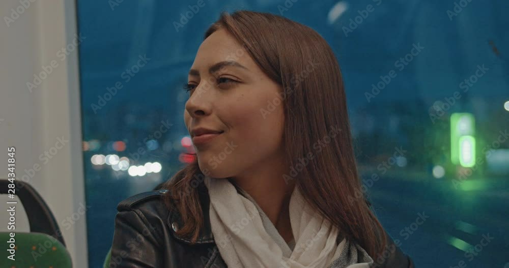 Portrait of young attractive smiling girl looking at camera during ride in public transport in evening in city lights. Car traffic on background. Night city, urban background. Portrait of young attractive smiling girl looking at camera during ride in public transport in evening in city lights. Car traffic on background. Night city, urban background.