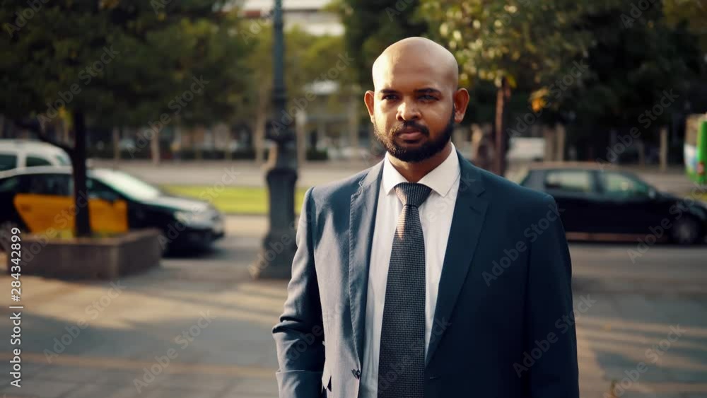 Indian businessman wearing blue suit standing with travel bag or suitcase near office or hotel. Travel business concept Indian businessman wearing blue suit standing with travel bag or suitcase near office or hotel. Travel business concept